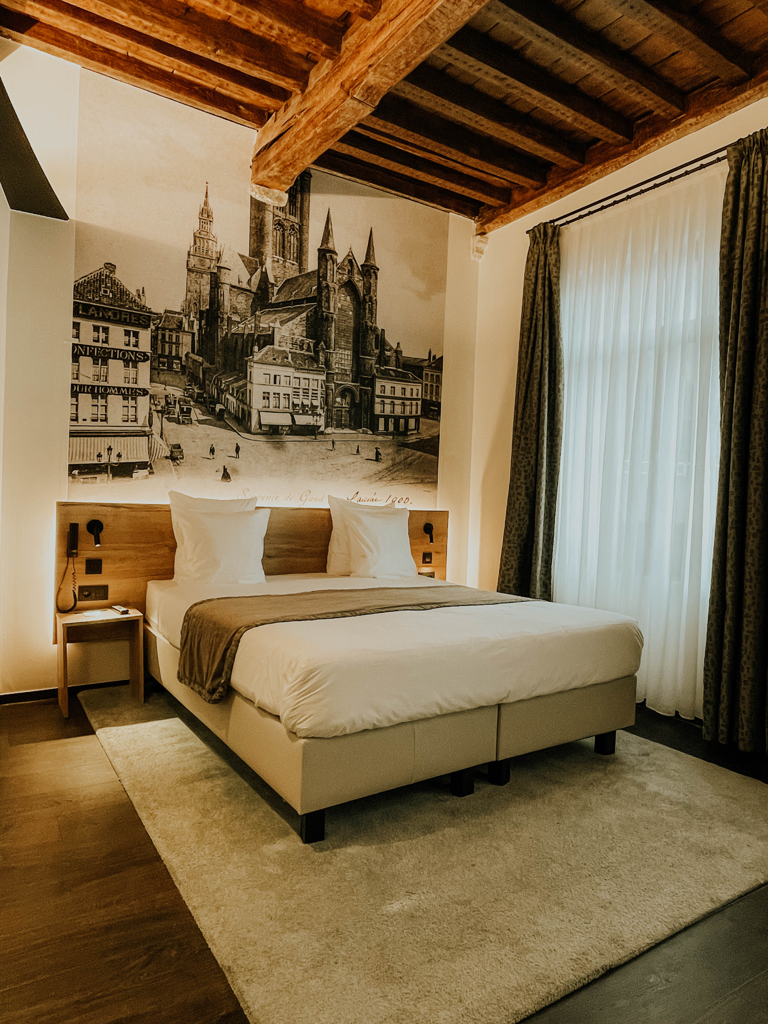 Luxe kamer met houten balken en een muurschildering van de Gentse binnenstad